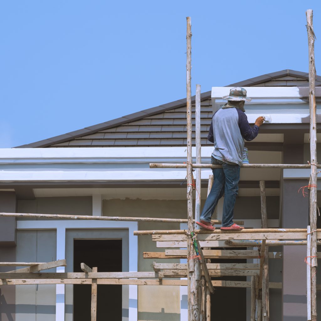 Asian builder worker on wooden scaffolding is painting roof structure of modern house